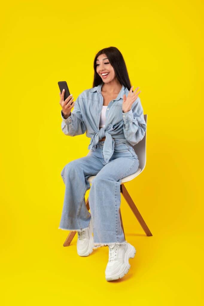 Cheerful woman having video call using cellphone and waving
