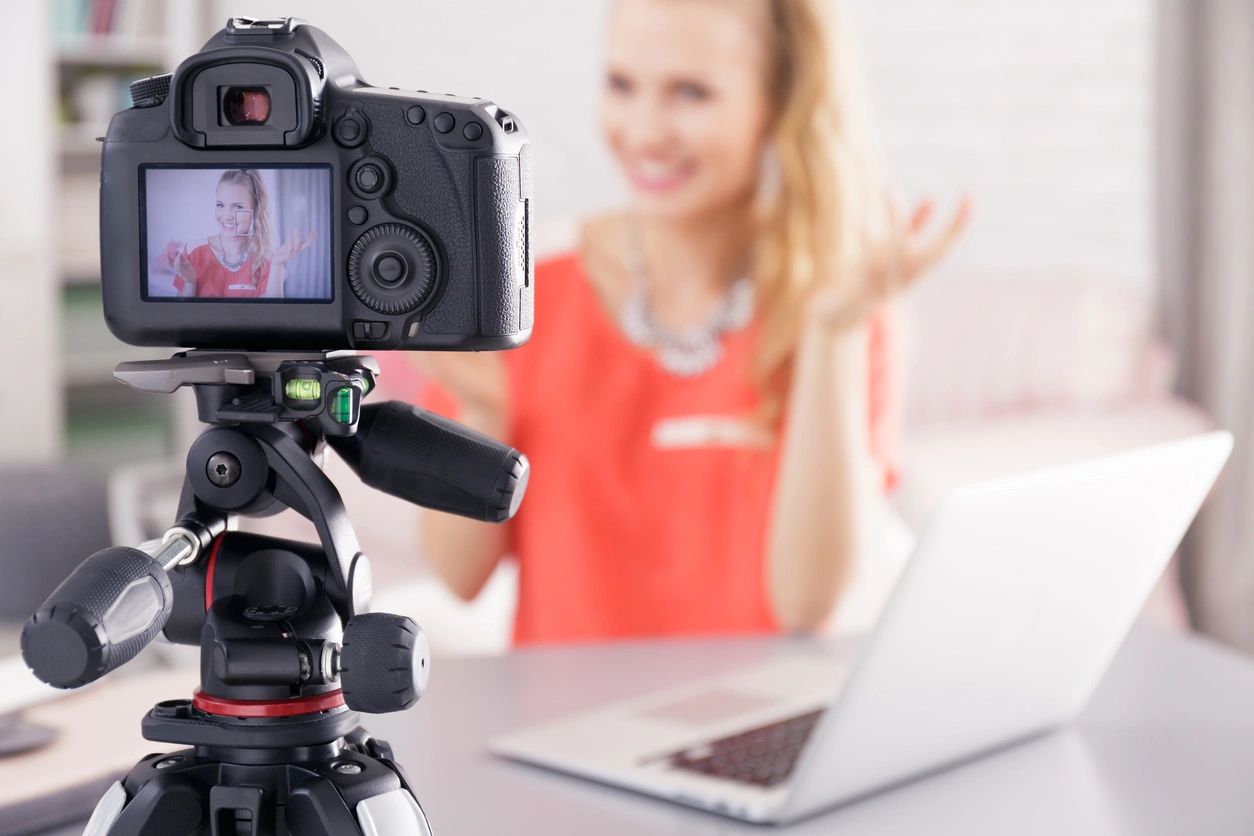 A woman with a laptop smiling at a video camera.