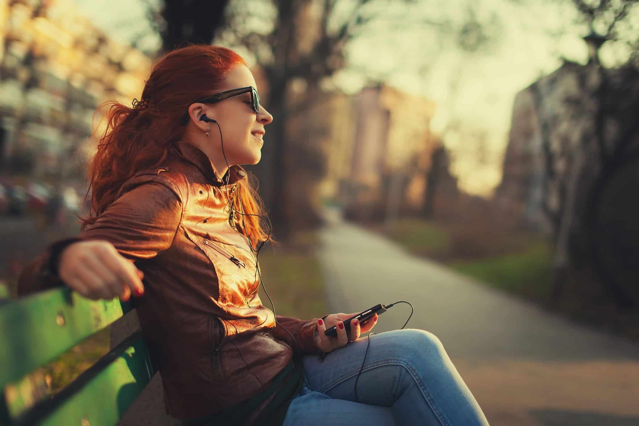 A woman sitting on a bench listening to music.