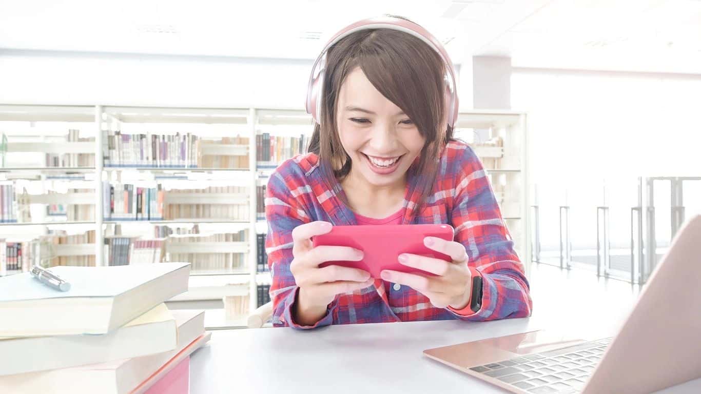 A young woman in a library playing a game on her phone.