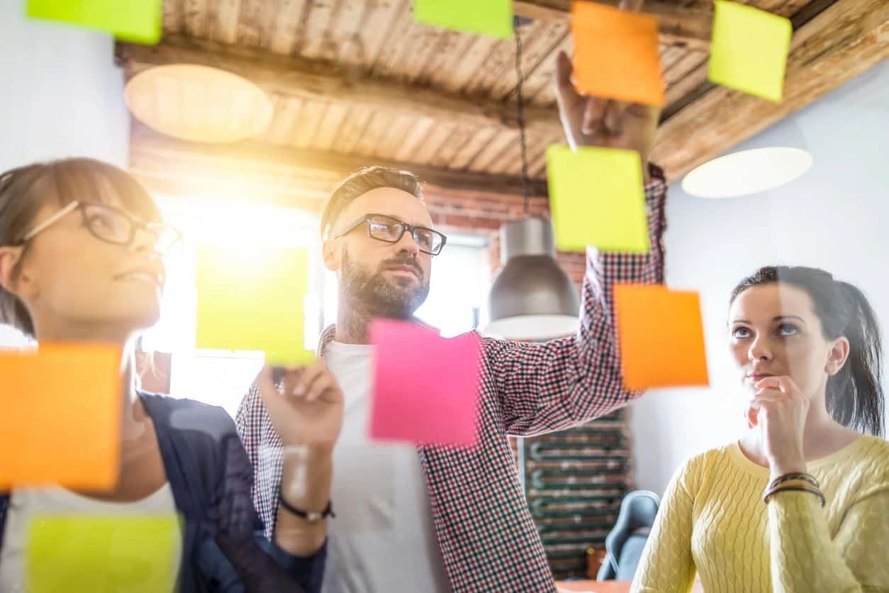 Three people in front of a glass wall with sticky notes on it.