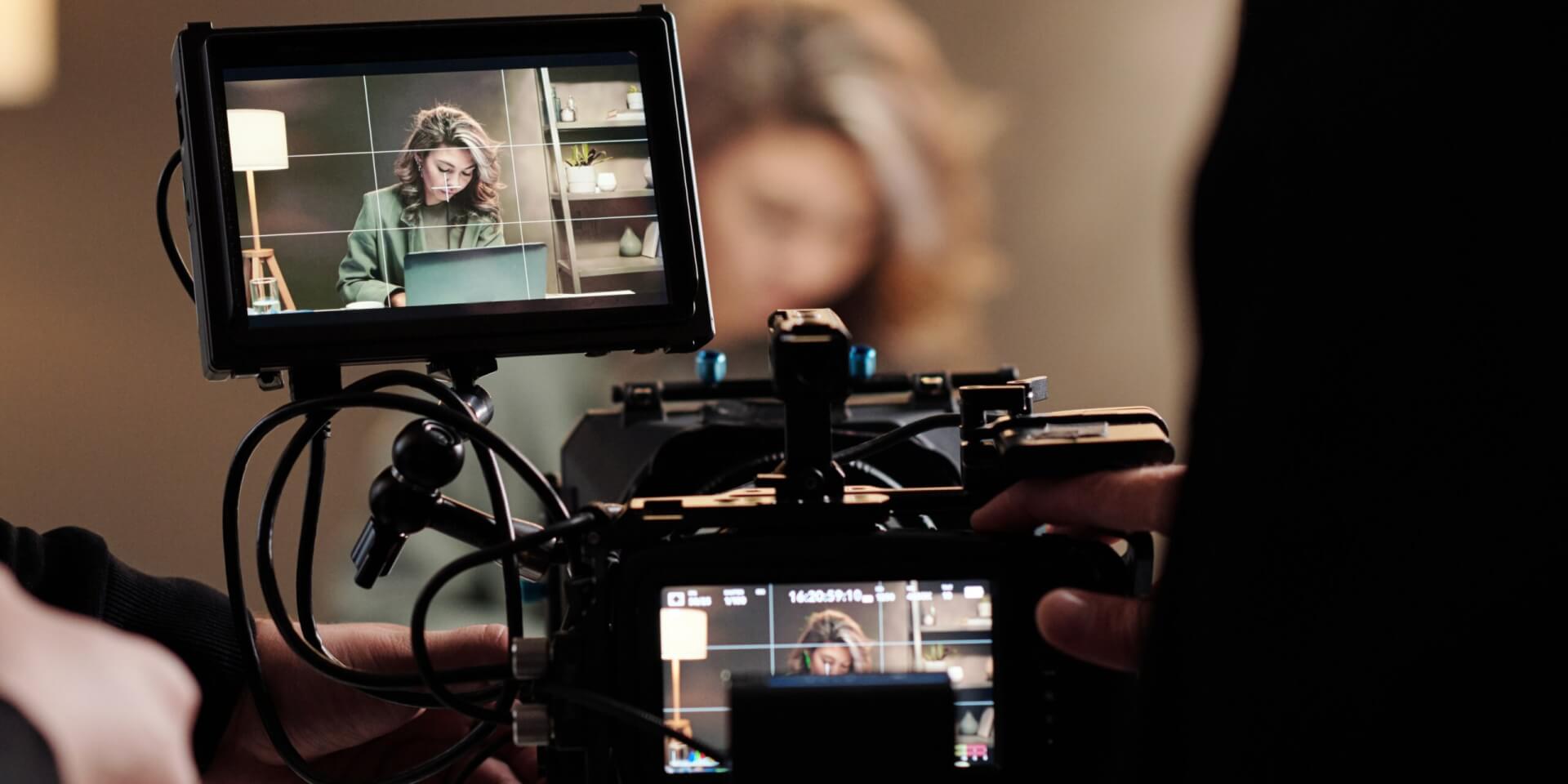 A video camera filming a woman on her laptop.