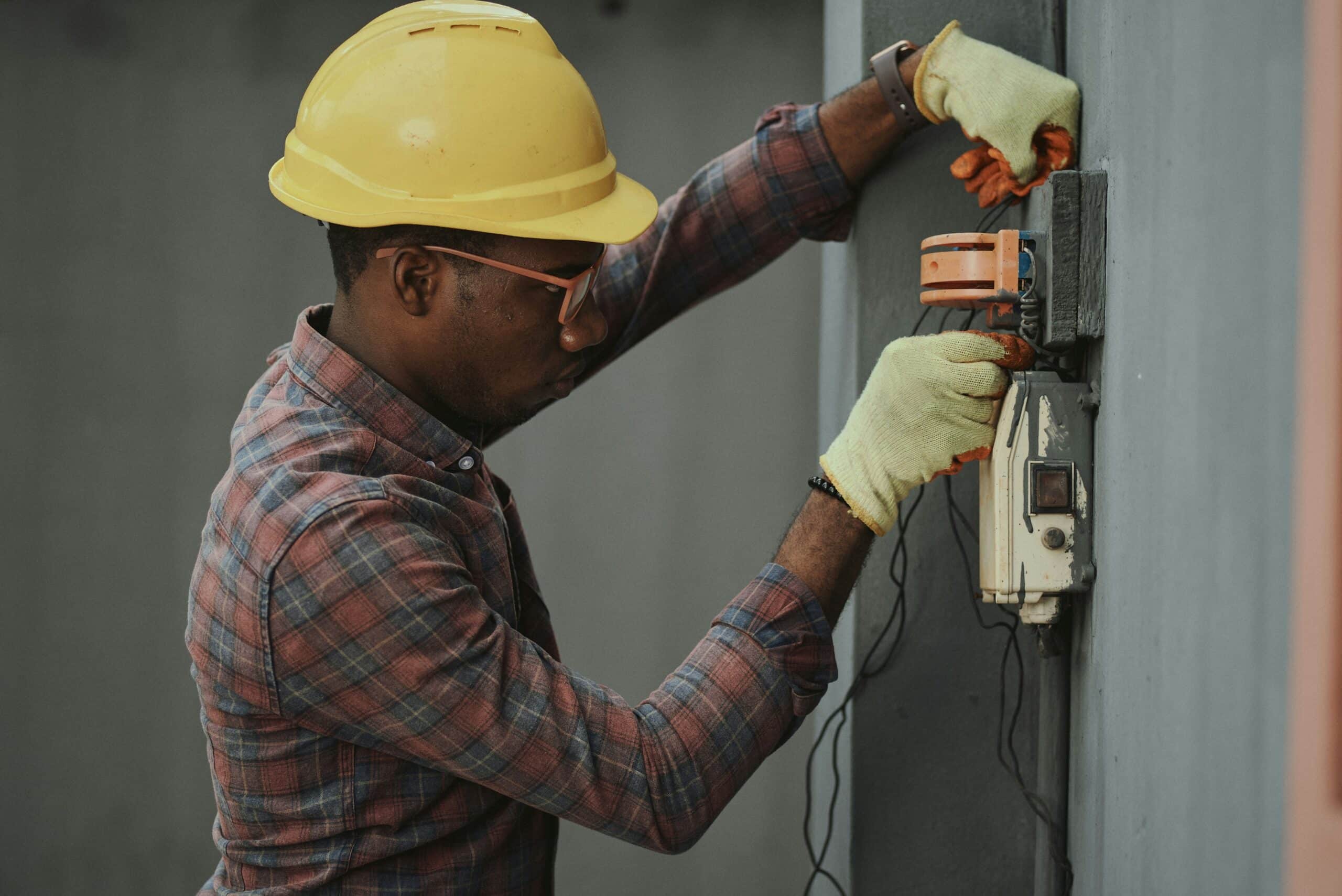 Man in brown and white shirt and yellow hard hat holding black and orange device